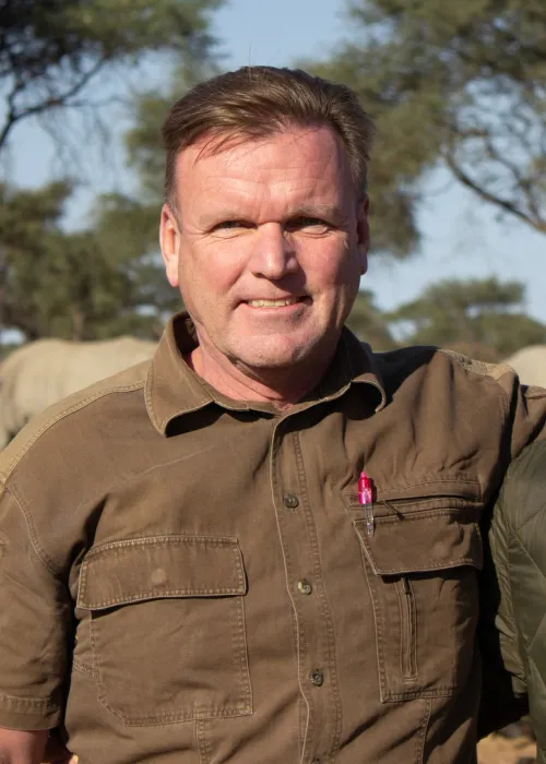 Portrait of a smiling man in a khaki shirt in front of acacia trees